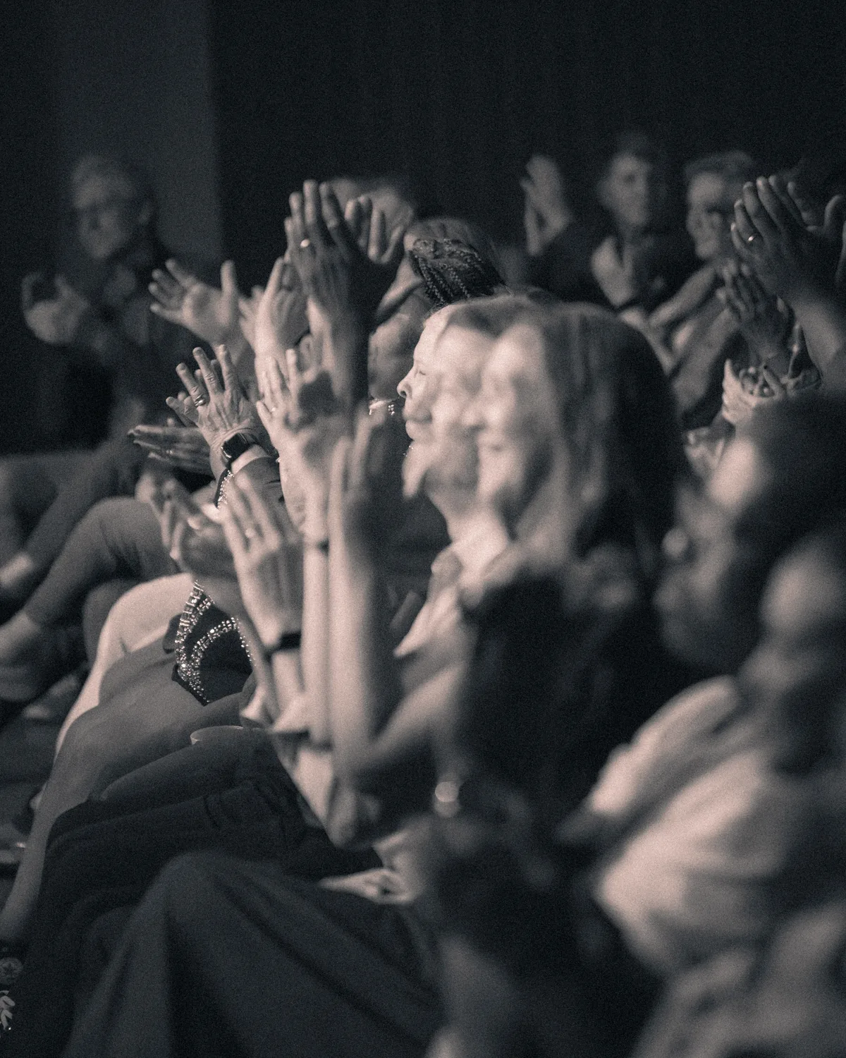 Concert audience members raising hands and applauding during live music performance