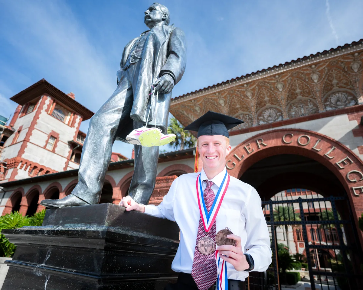 Flagler College graduate posing by the Ponce de Leon statue at campus entrance