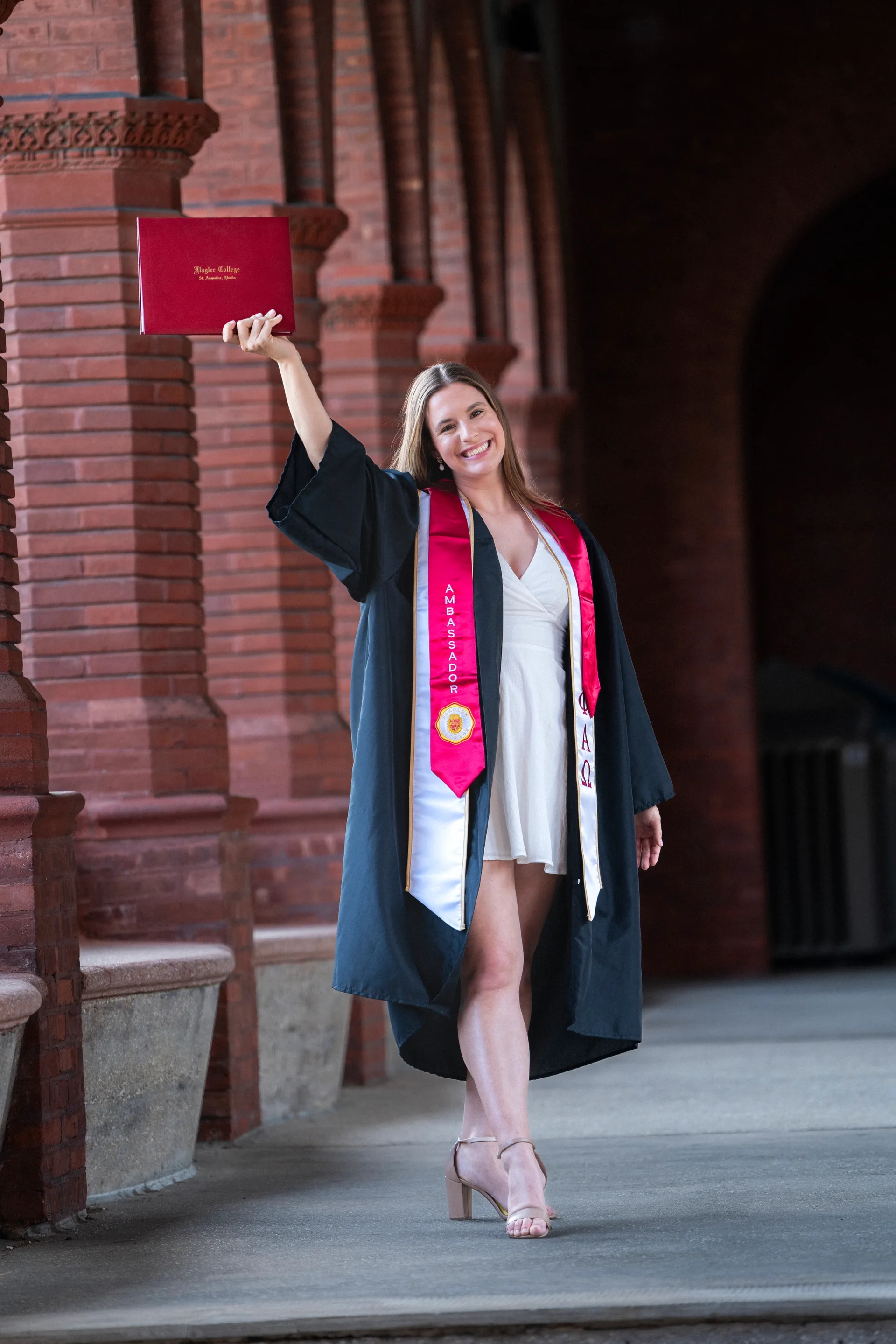 Flagler College graduate celebrating with diploma raised in front of historic brick columns