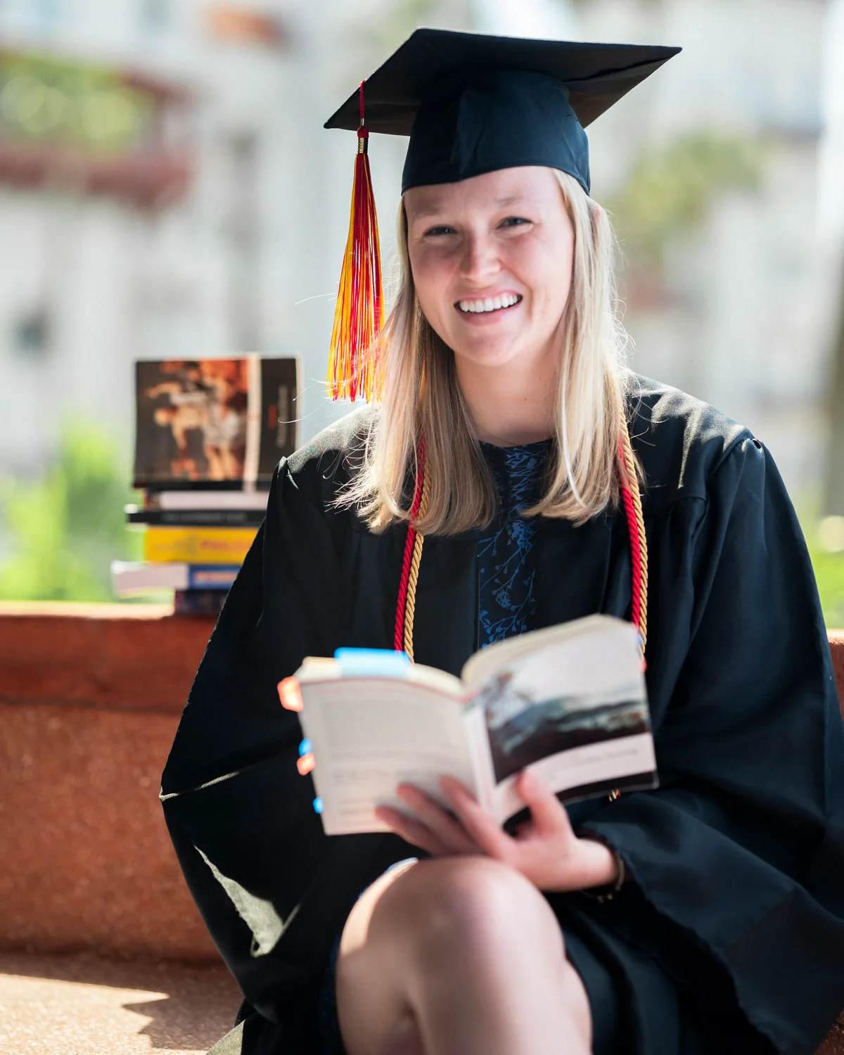 Flagler College honors graduate in cap and gown reading a book beside a stack of books on the historic St. Augustine campus — First Sight Films