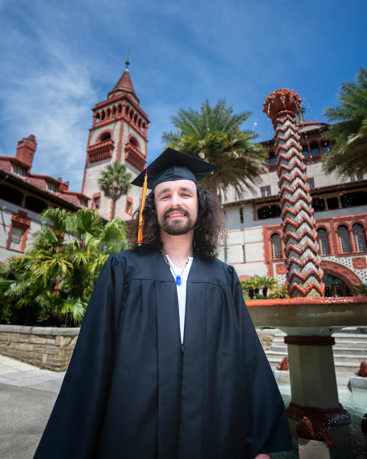 Flagler College graduate in cap and gown in the Ponce Hall courtyard, with the tower and ornate fountain behind, in St. Augustine — First Sight Films