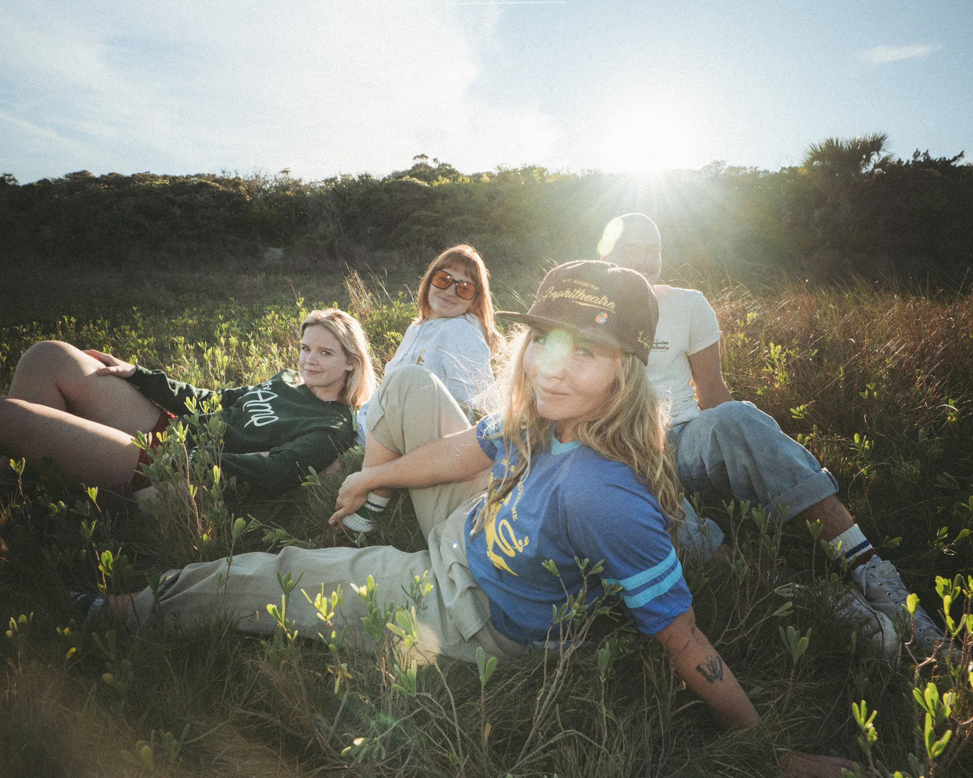 Group of models wearing St Augustine Amphitheatre merch lounging in grass at golden hour