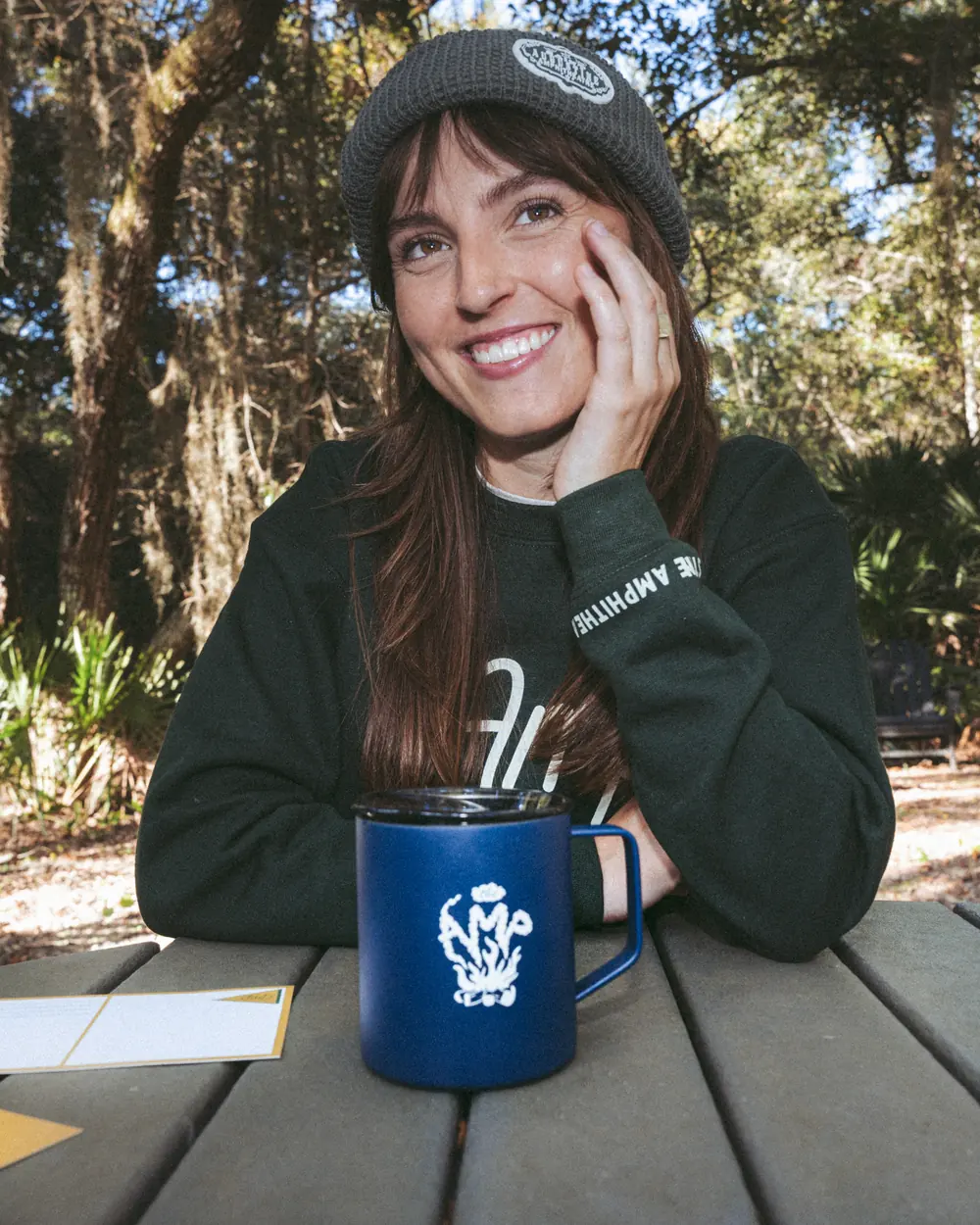 Lifestyle apparel photography — woman in a St. Augustine Amphitheatre beanie and crewneck with an AMP camp mug